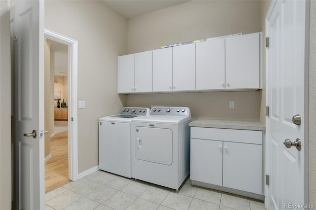 washroom featuring washing machine and dryer, cabinets, and light tile patterned floors