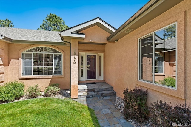 19770 Roaming Dr, Colorado Springs, CO 80908 - view of exterior entry with stucco siding, a shingled roof, and a yard