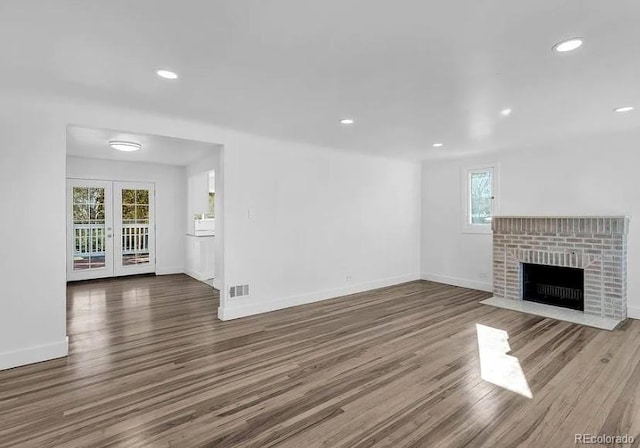 unfurnished living room featuring a brick fireplace, wood finished floors, and visible vents