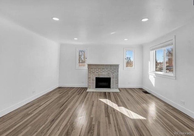 unfurnished living room with visible vents, baseboards, a brick fireplace, and wood finished floors