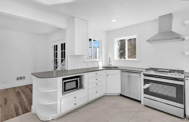 kitchen with visible vents, a sink, white cabinets, appliances with stainless steel finishes, and wall chimney exhaust hood