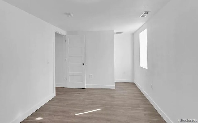 empty room with wood finished floors, visible vents, and baseboards