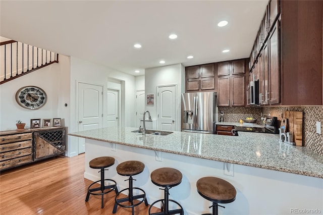 kitchen with sink, stainless steel appliances, light stone counters, tasteful backsplash, and kitchen peninsula