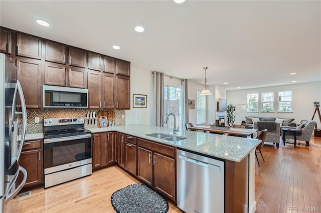 kitchen featuring sink, light hardwood / wood-style flooring, stainless steel appliances, decorative light fixtures, and kitchen peninsula