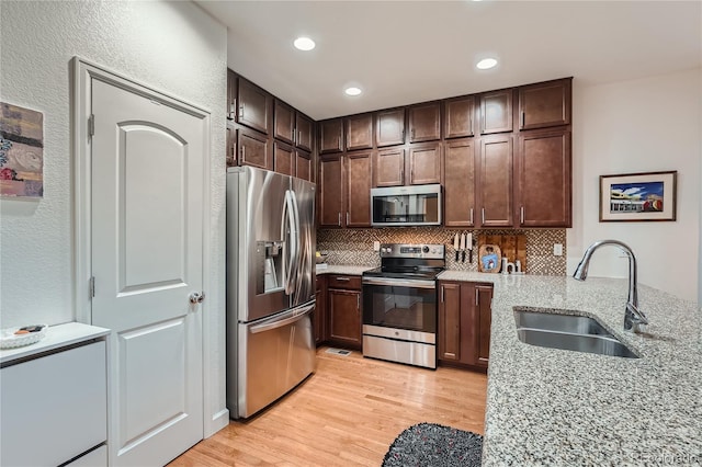 kitchen with sink, tasteful backsplash, appliances with stainless steel finishes, light stone countertops, and light hardwood / wood-style floors