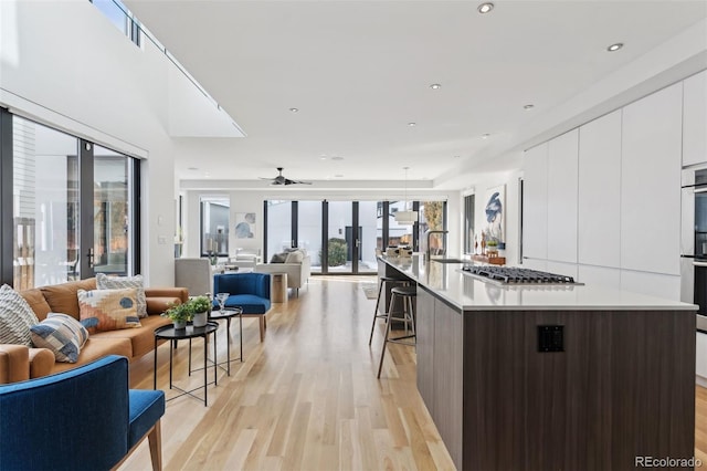 kitchen with white cabinetry, light hardwood / wood-style floors, a kitchen breakfast bar, a center island with sink, and dark brown cabinets