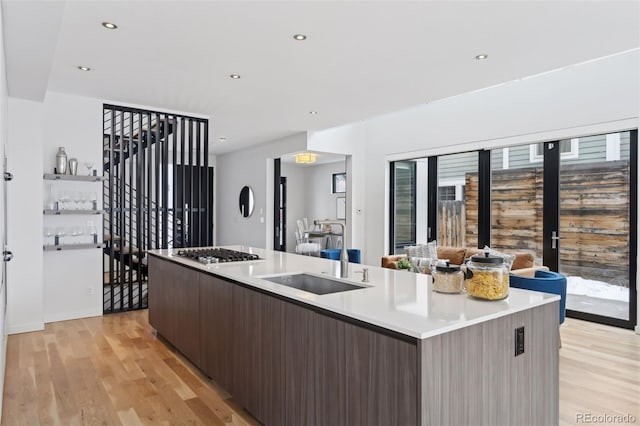 kitchen featuring dark brown cabinetry, an island with sink, light hardwood / wood-style floors, sink, and stainless steel gas stovetop