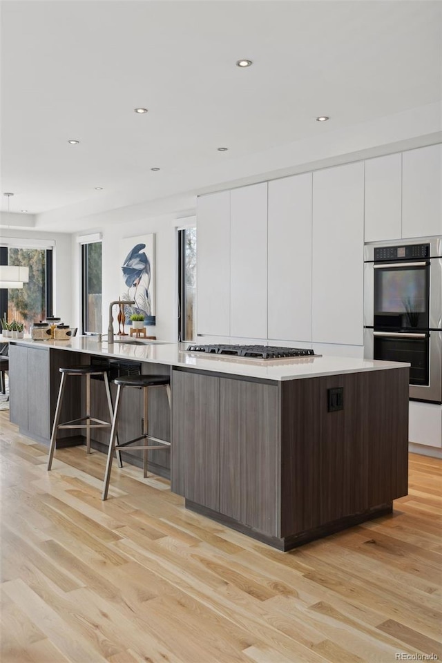 kitchen with light hardwood / wood-style floors, white cabinetry, appliances with stainless steel finishes, and a large island