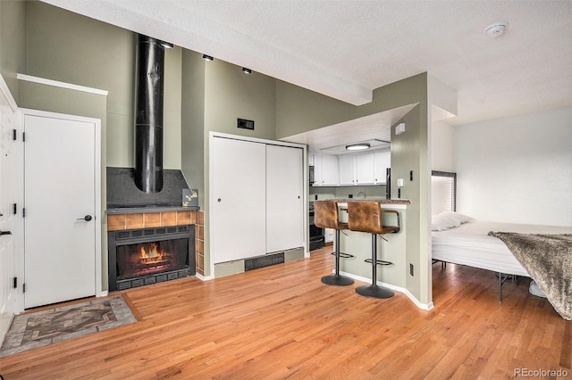 living room with light wood-type flooring, a textured ceiling, a fireplace, a towering ceiling, and beam ceiling