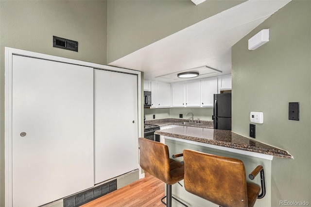 kitchen with white cabinetry, sink, dark stone counters, a kitchen bar, and black appliances