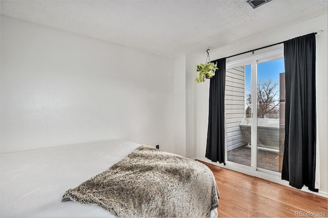 bedroom with access to outside, a textured ceiling, and hardwood / wood-style flooring