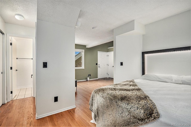 bedroom with lofted ceiling, light wood-type flooring, and a textured ceiling