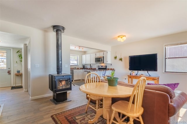 dining space featuring light wood-style floors, a wood stove, and baseboards