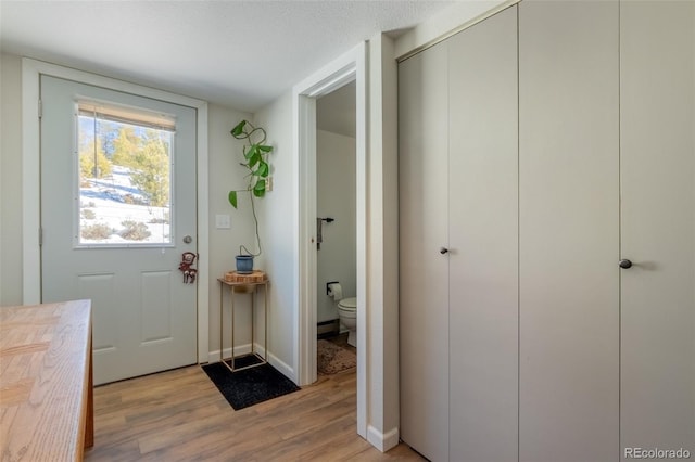 doorway to outside featuring a textured ceiling, baseboard heating, light wood-style flooring, and baseboards