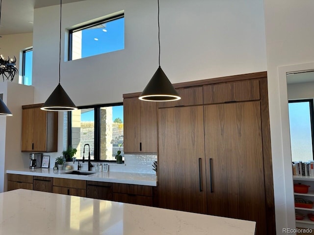 kitchen featuring decorative light fixtures, light stone countertops, sink, and a high ceiling