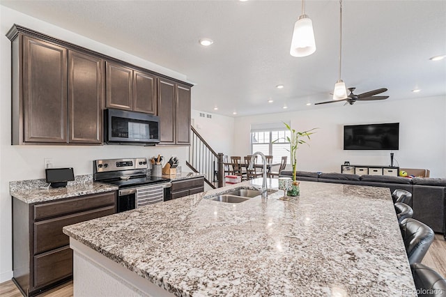 kitchen with sink, stainless steel range with electric stovetop, dark brown cabinets, light stone countertops, and decorative light fixtures