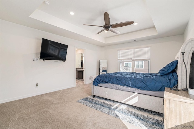 bedroom with ceiling fan, carpet flooring, ensuite bath, and a tray ceiling