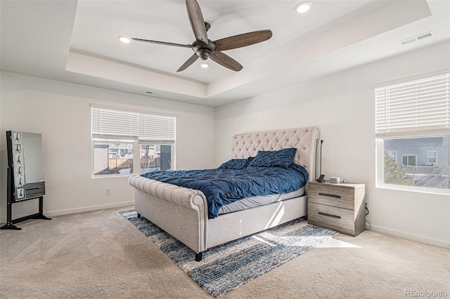 bedroom with light carpet, a tray ceiling, and ceiling fan