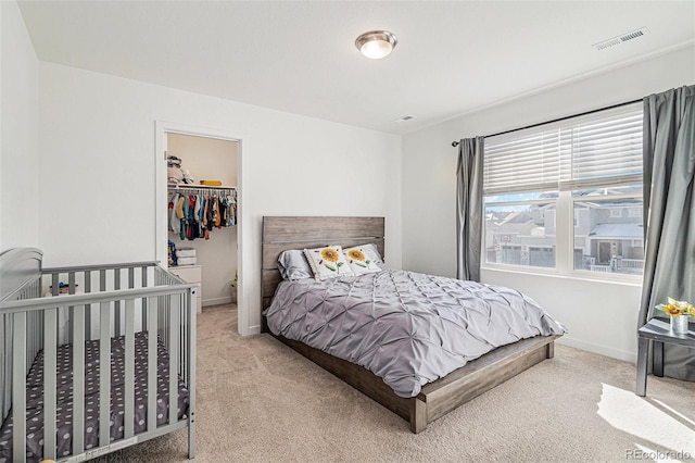 bedroom with a walk in closet, a closet, and light carpet