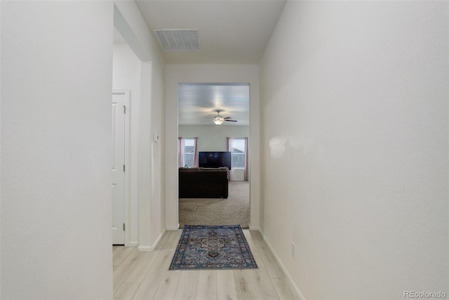 hallway featuring visible vents, baseboards, and wood finished floors