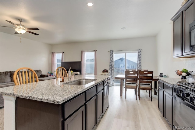 kitchen with light stone counters, open floor plan, a sink, gas range, and light wood-type flooring