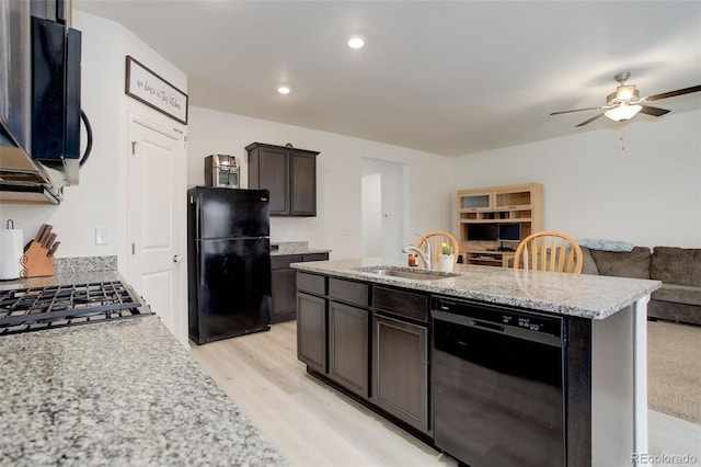 kitchen with a sink, open floor plan, black appliances, light wood finished floors, and an island with sink