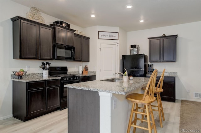 kitchen with light stone countertops, black appliances, a breakfast bar, and a sink