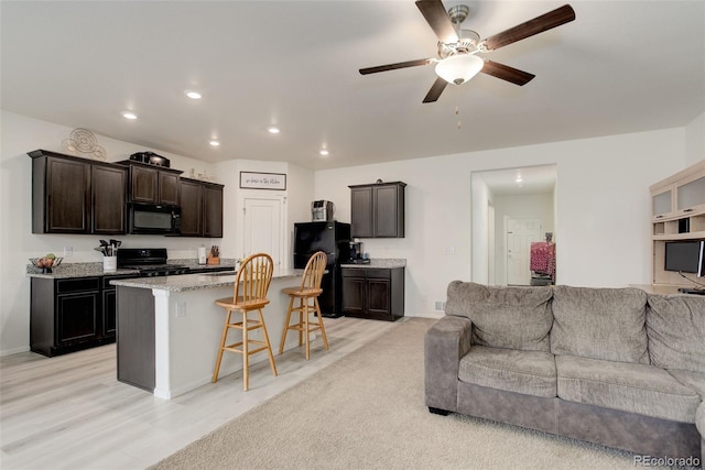 kitchen featuring recessed lighting, open floor plan, black appliances, a kitchen bar, and a center island with sink