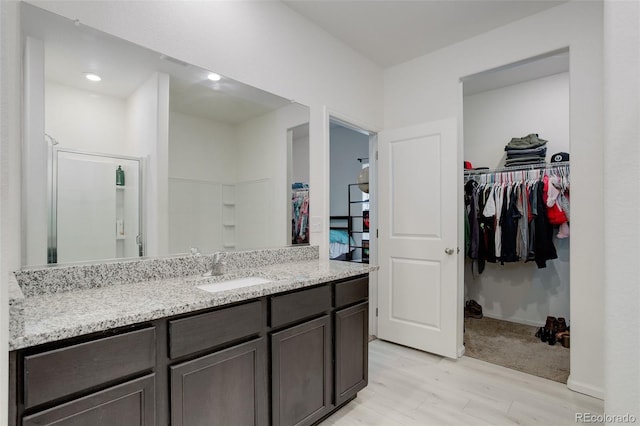 full bathroom featuring wood finished floors, vanity, baseboards, a spacious closet, and walk in shower