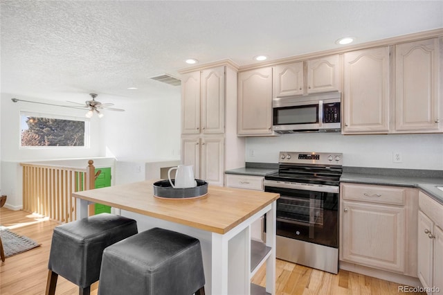 kitchen with light hardwood / wood-style flooring, ceiling fan, appliances with stainless steel finishes, butcher block counters, and a textured ceiling