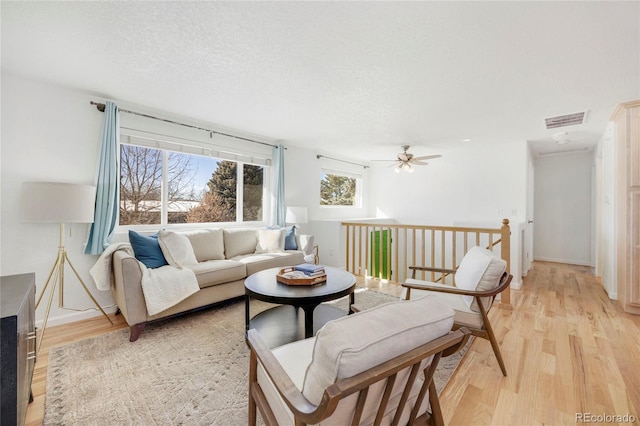 living room with ceiling fan, light hardwood / wood-style floors, and a textured ceiling