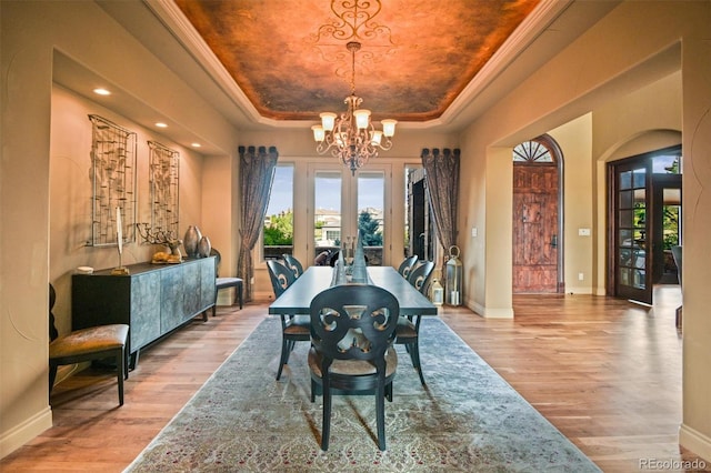 dining space with french doors, a tray ceiling, a chandelier, and light wood-type flooring