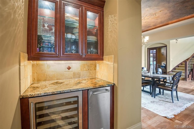 bar with backsplash, light stone countertops, beverage cooler, and light hardwood / wood-style floors