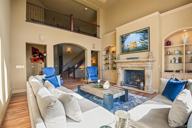 living room featuring light hardwood / wood-style flooring, a towering ceiling, built in shelves, a premium fireplace, and ornamental molding