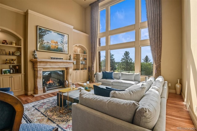 living room with crown molding, light hardwood / wood-style floors, built in features, and a towering ceiling