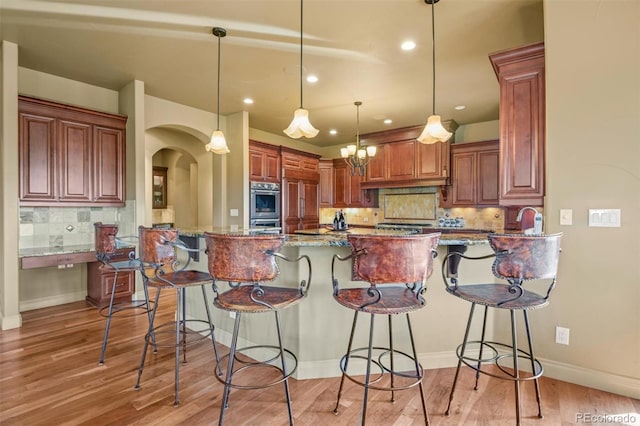 kitchen featuring stone counters, stainless steel double oven, light wood-type flooring, and tasteful backsplash