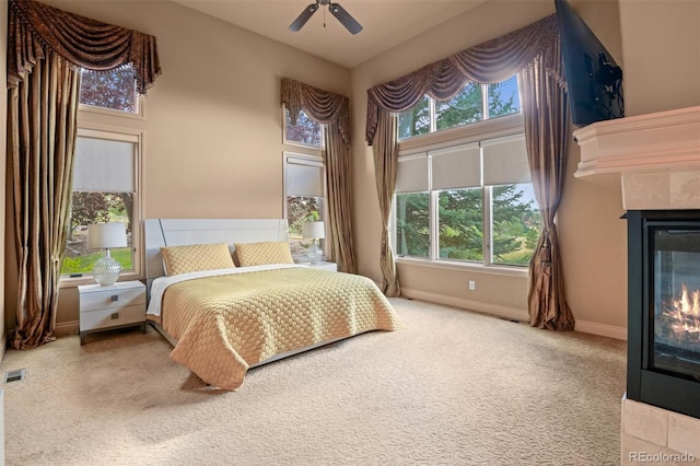 bedroom featuring ceiling fan, light carpet, multiple windows, and a tile fireplace