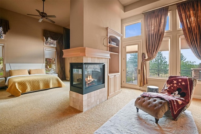 sitting room with light colored carpet, built in features, ceiling fan, a high ceiling, and a tiled fireplace