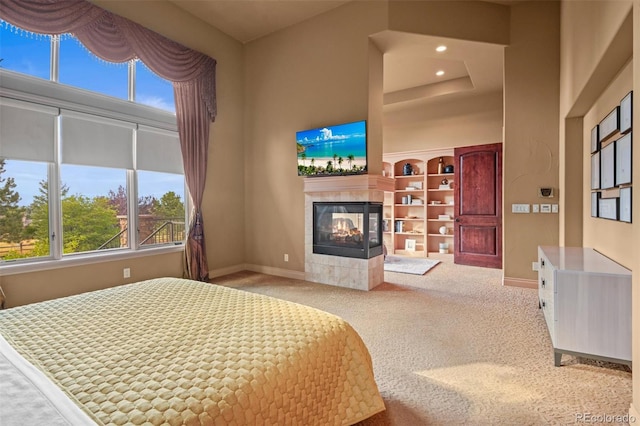 bedroom with light colored carpet, multiple windows, a tile fireplace, and a towering ceiling