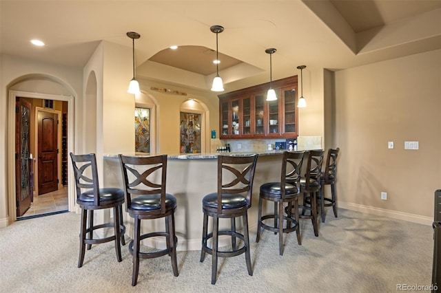 bar featuring light carpet, a tray ceiling, light stone counters, and pendant lighting