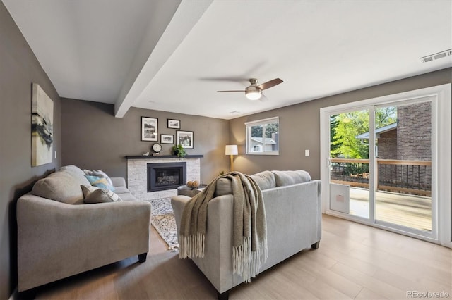 10909 W 65th Way, Arvada, CO 80004 - living room with a ceiling fan, a glass covered fireplace, beamed ceiling, and light wood-type flooring