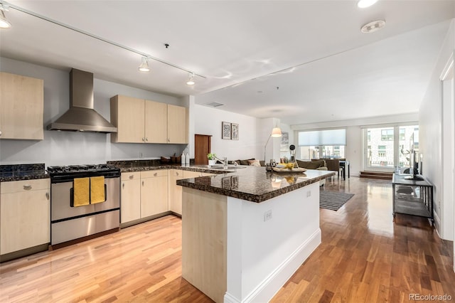 kitchen featuring light hardwood / wood-style floors, sink, stainless steel range with gas stovetop, light brown cabinets, and wall chimney exhaust hood