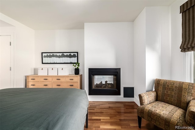 bedroom with a multi sided fireplace and dark wood-type flooring