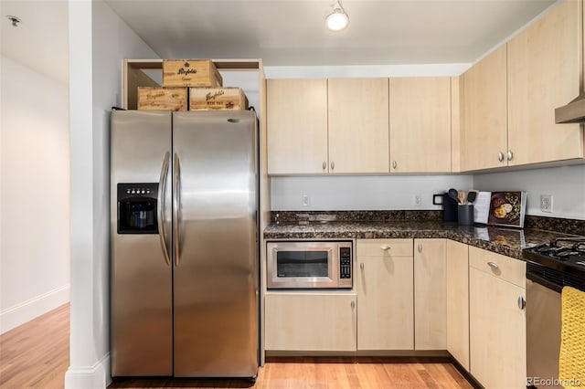 kitchen featuring stainless steel appliances, light brown cabinetry, dark stone countertops, and light hardwood / wood-style flooring