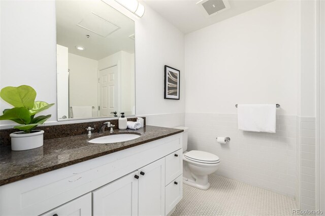 bathroom featuring toilet, tile patterned flooring, tile walls, and vanity