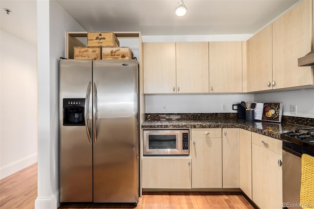 kitchen featuring appliances with stainless steel finishes, dark stone counters, light brown cabinetry, and light hardwood / wood-style flooring