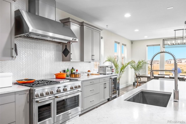 kitchen featuring decorative light fixtures, wall chimney range hood, beverage cooler, tasteful backsplash, and double oven range