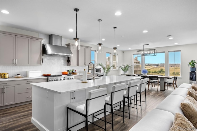 kitchen with a kitchen island with sink, a breakfast bar, sink, and wall chimney range hood