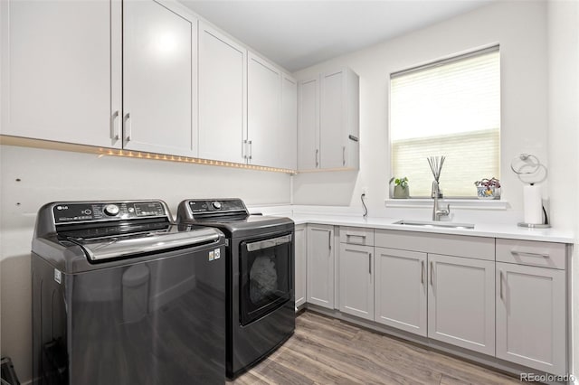 clothes washing area featuring separate washer and dryer, light hardwood / wood-style flooring, cabinets, and sink