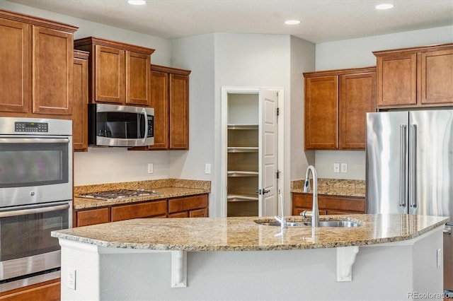 kitchen featuring appliances with stainless steel finishes, sink, light stone countertops, and an island with sink